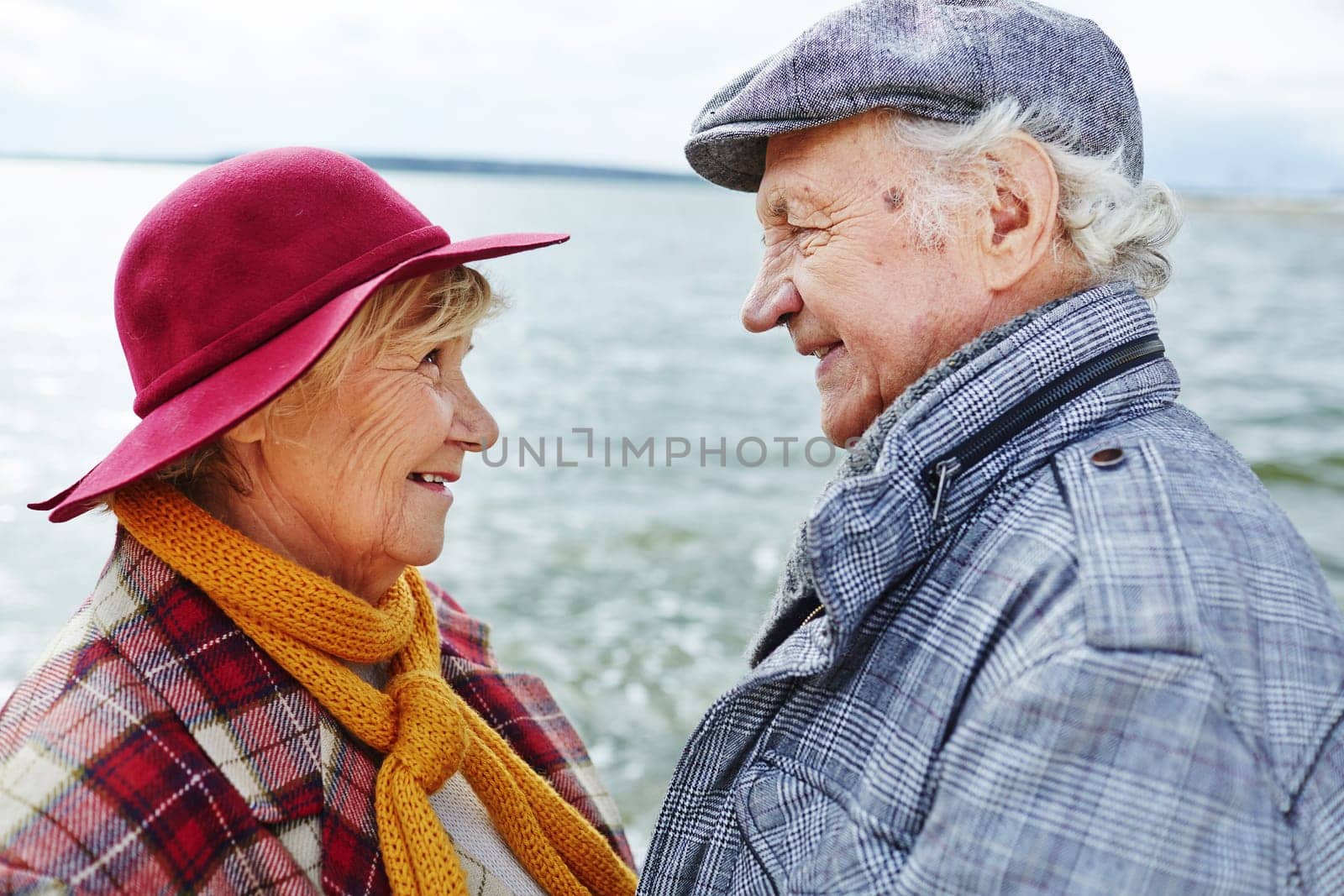Retired couple in warm clothes looking at one another by seaside