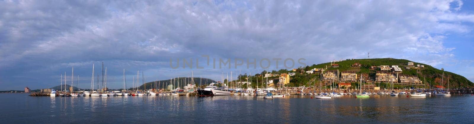 Summer coast panorama with boats in pier and cloudy skyline hill view of Piriapolis, Uruguay from the sea.