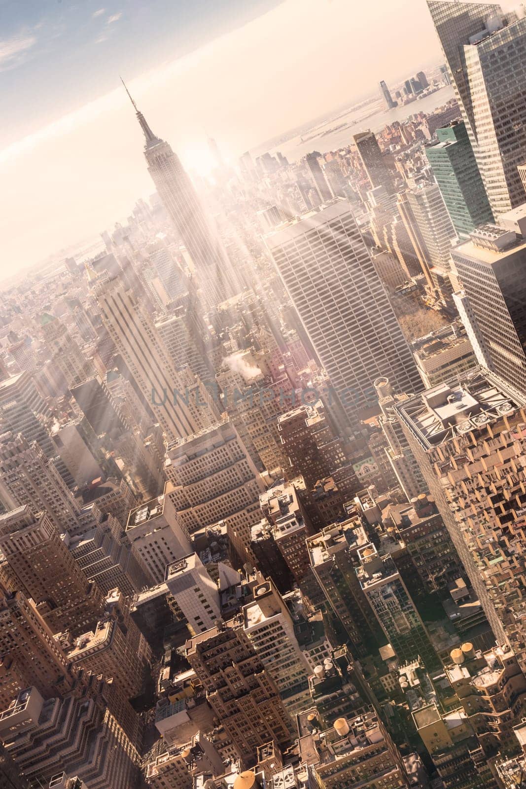 New York City. Manhattan downtown skyline with illuminated Empire State Building and skyscrapers at sunset. Vertical composition. Warm evening colors. Sunbeams and lens flare.