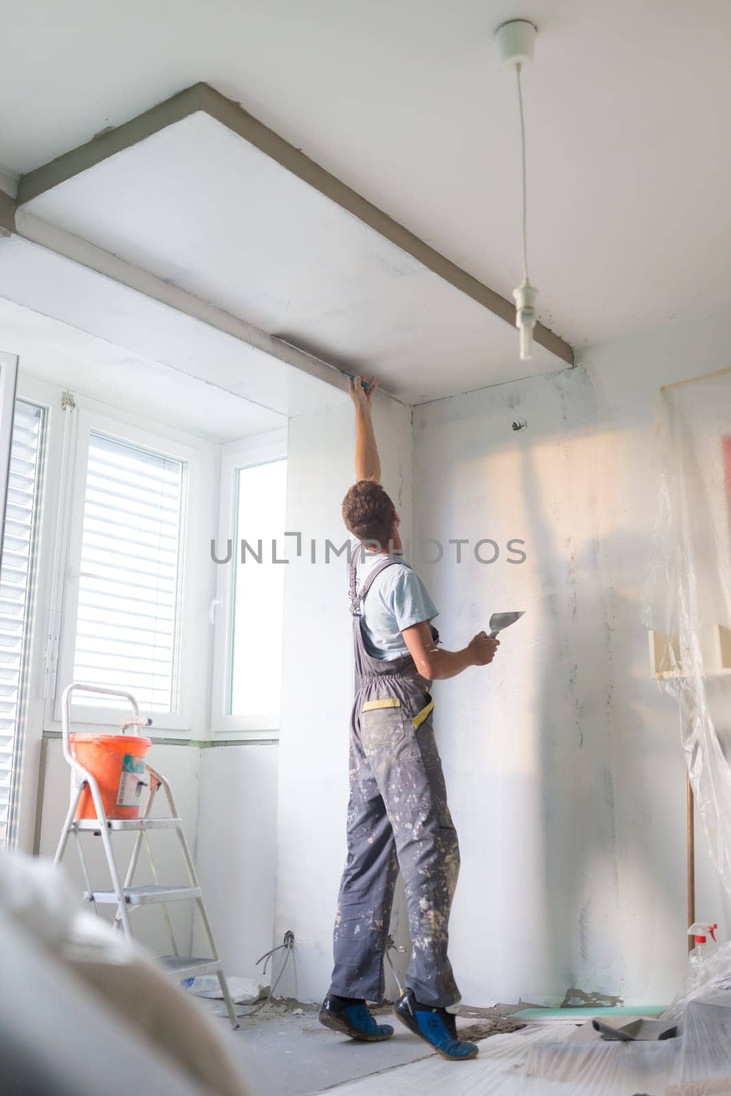 Thirty years old manual worker with wall plastering tools inside a house. Plasterer renovating indoor walls and ceilings with float and plaster.