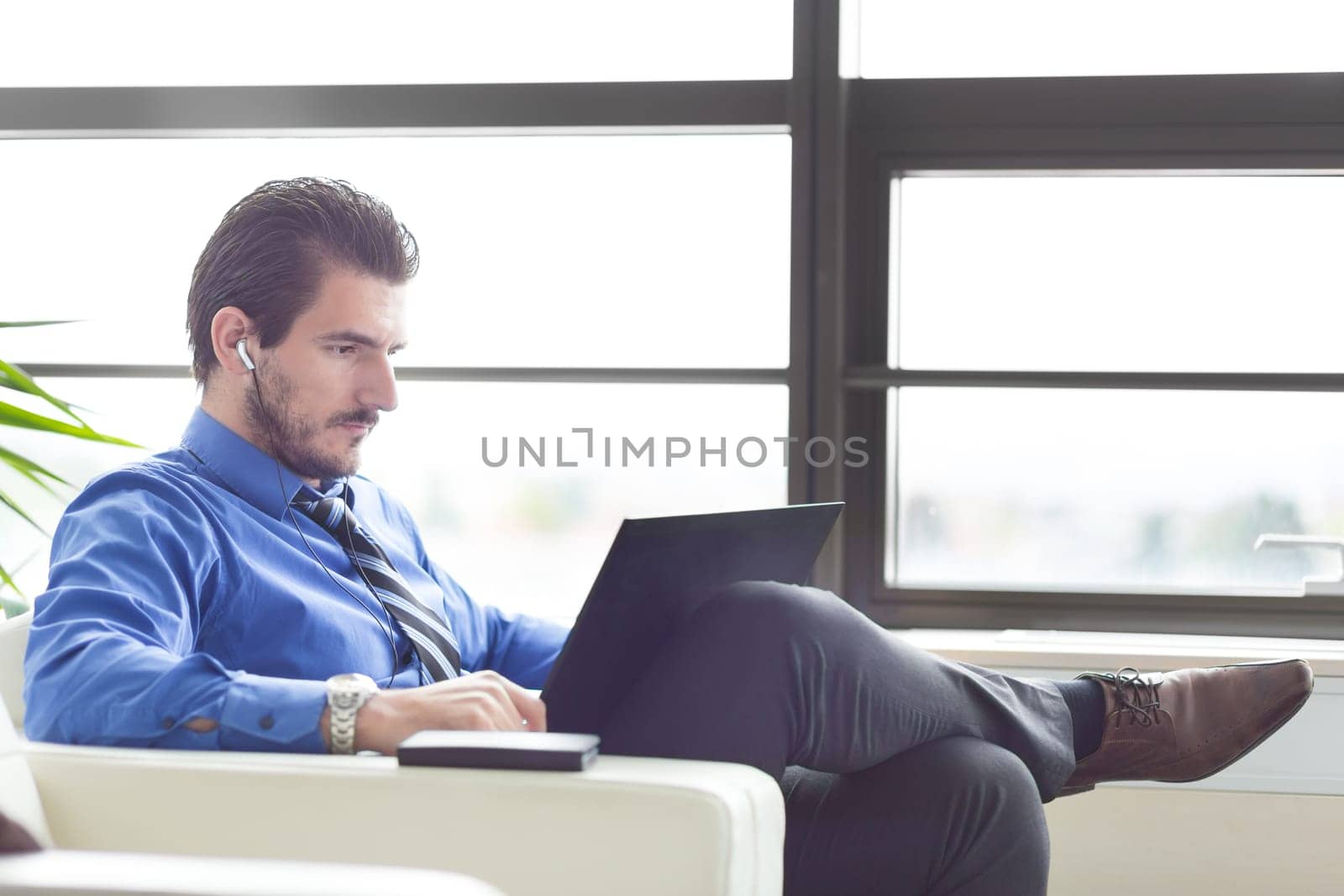 Busy, focused businessman in office working on his laptop wearing headphones. Side view.