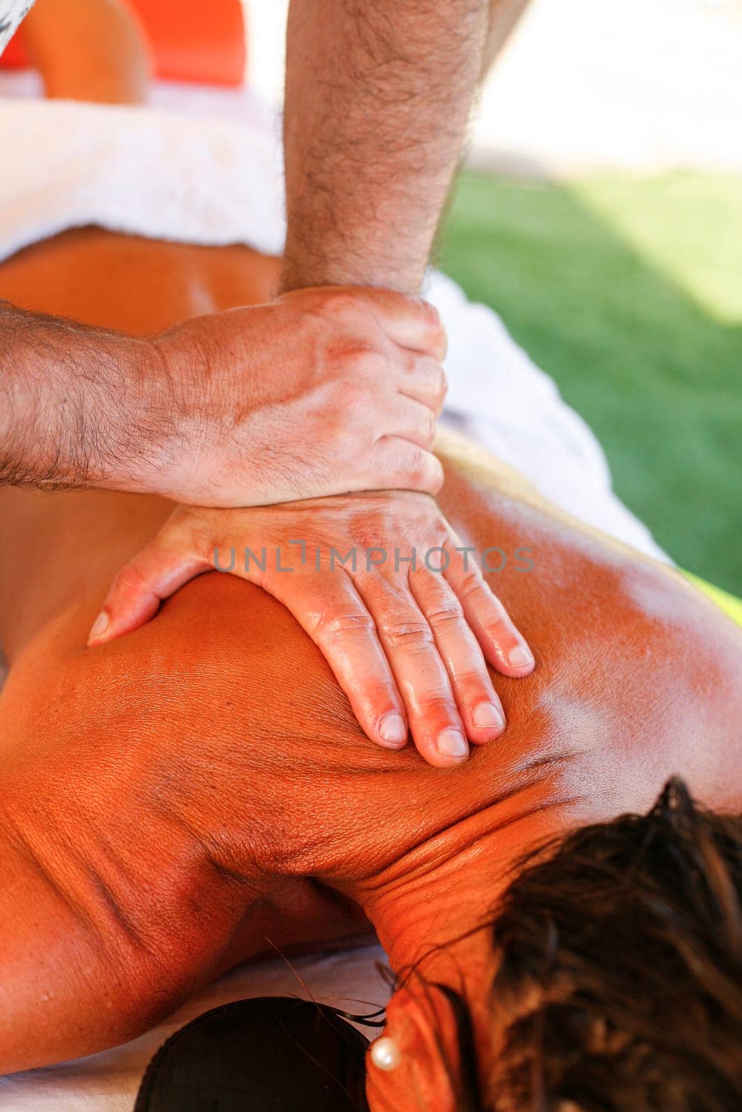 Massage therapist working with suntanned beautiful woman at  beach resort