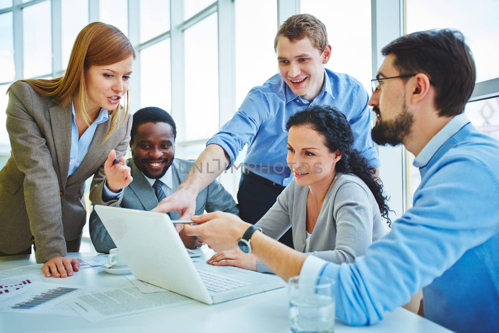 Group of employees looking at data in laptop and voicing their ideas at meeting