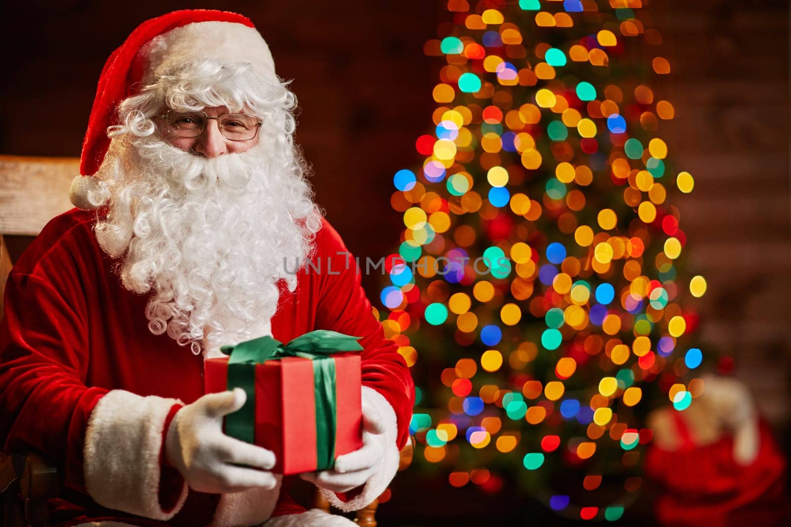 Santa Claus with giftbox on background of sparkling firtree