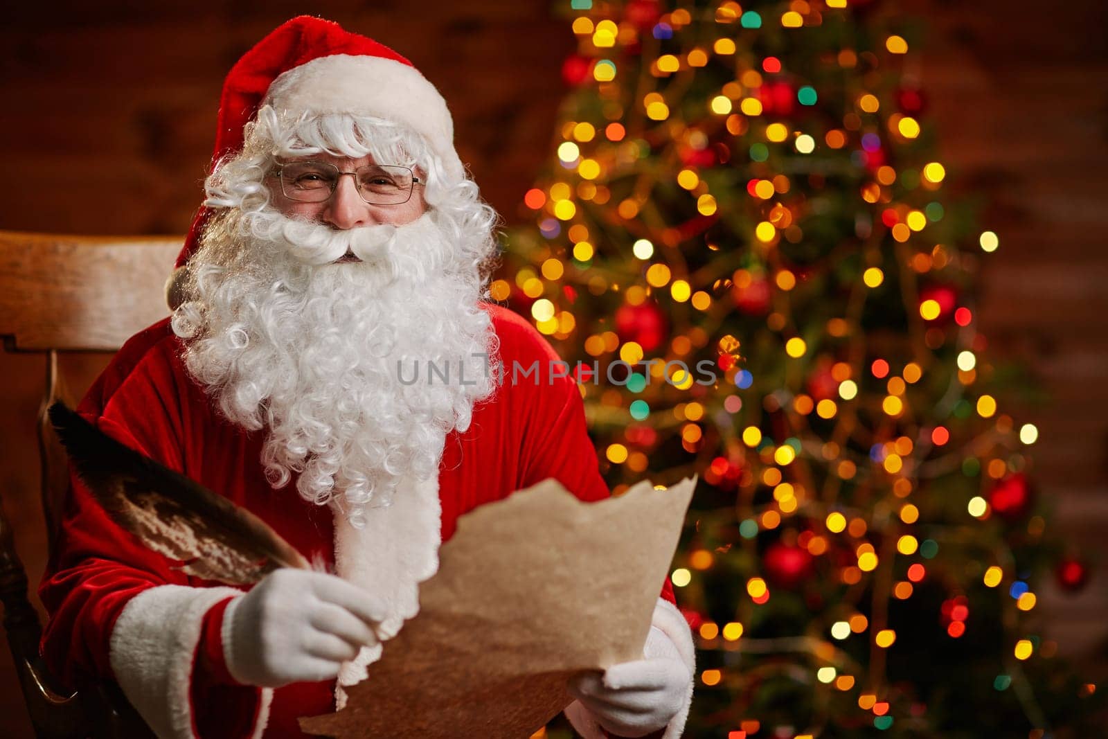 Senior man in costume of Santa Claus holding feather and Christmas letter