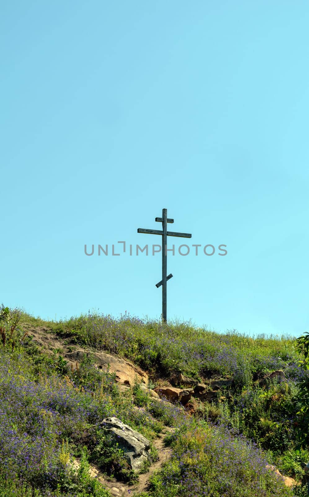 Big old wooden Orthodox cross on a hill on a clear blue cloudless sky on a summer day