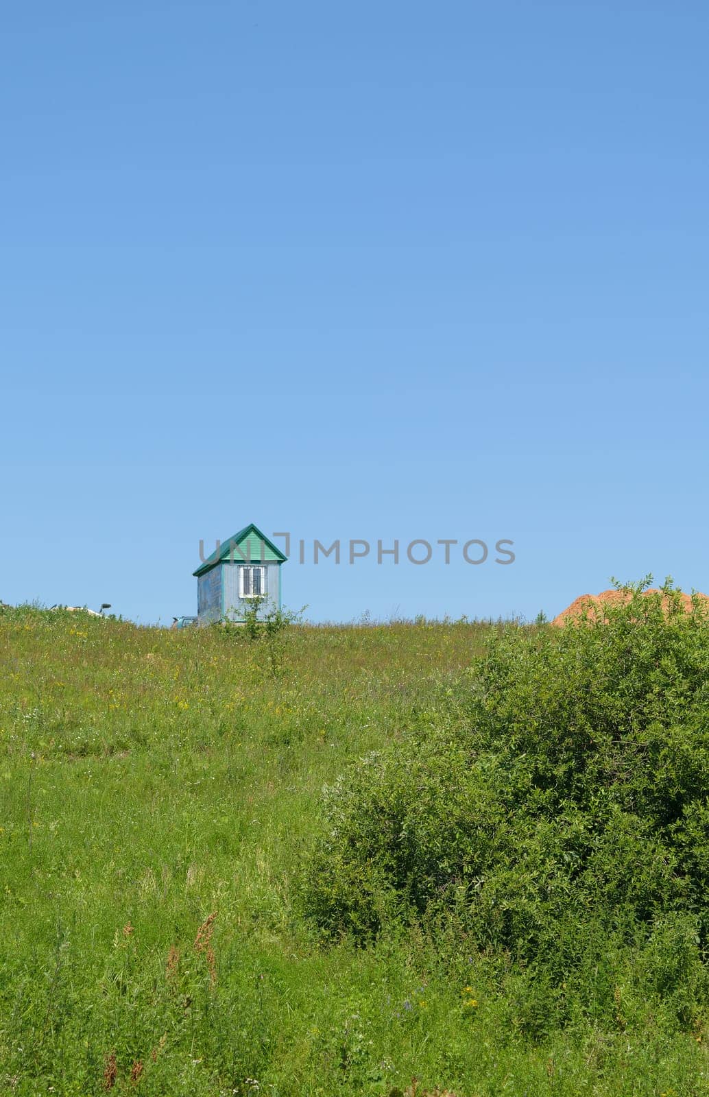A lone house stands on a green grass hill.