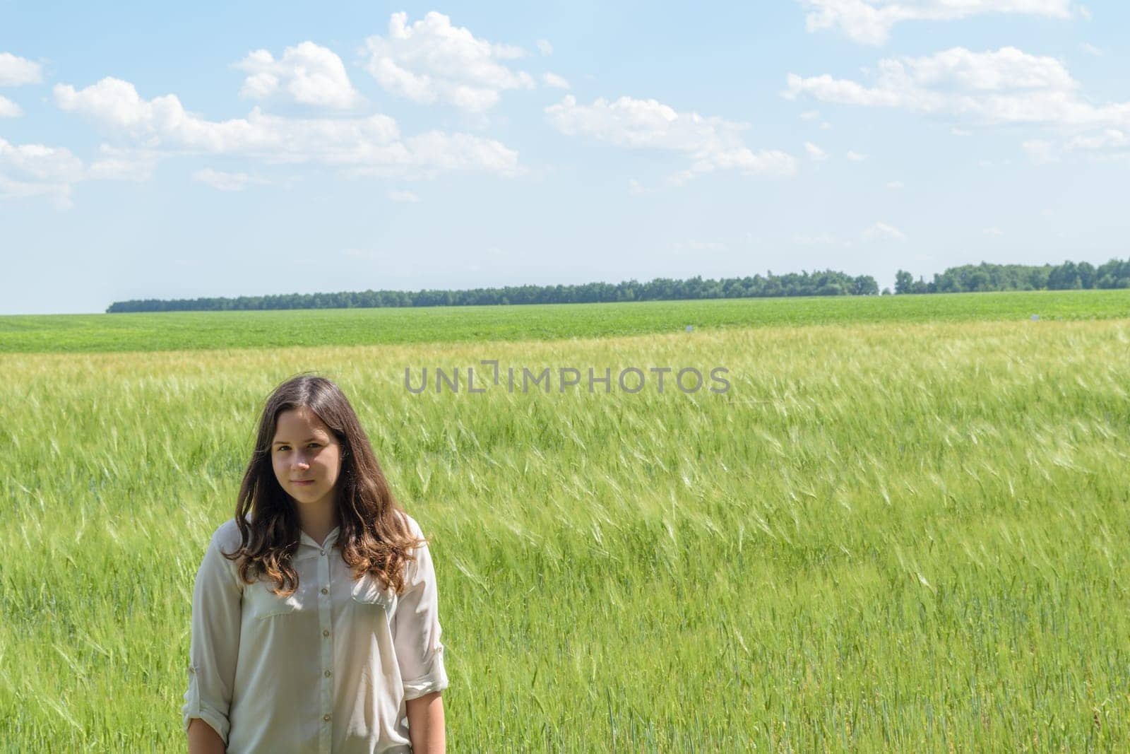 Young seventeen year old girl standing on a background of green field on a summer day.