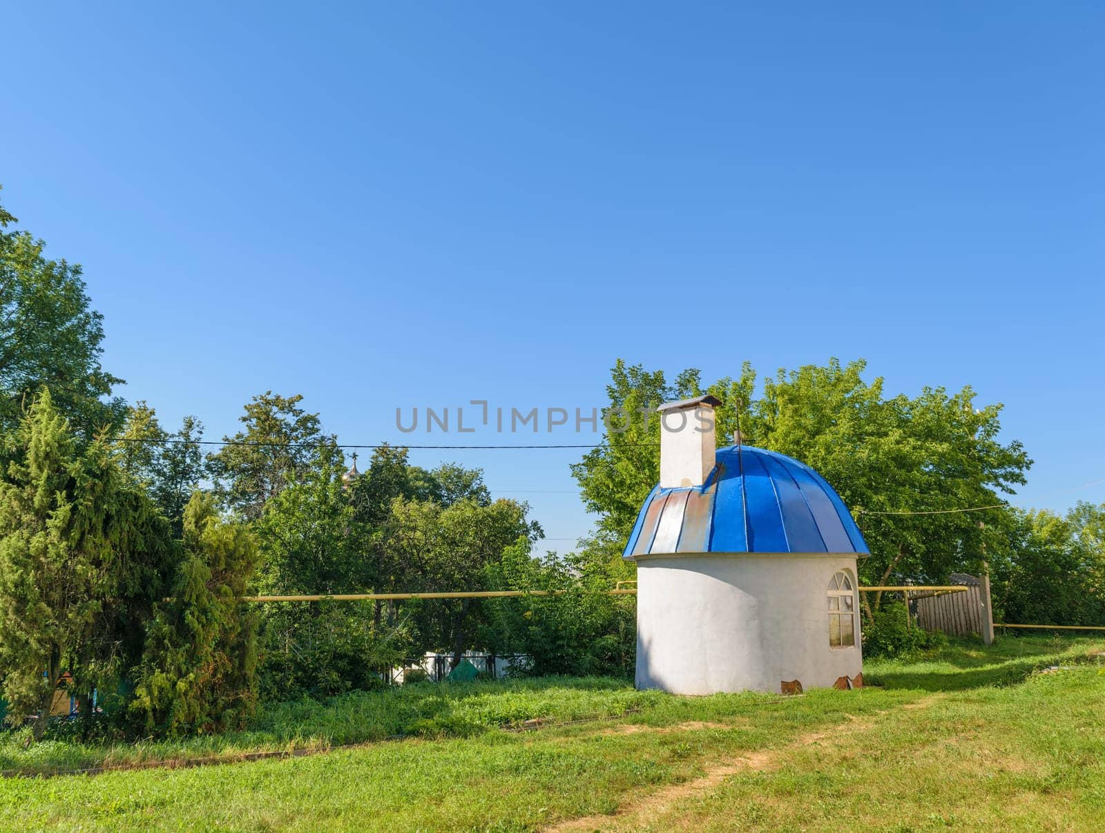 Small round house with blue domed roof on green lawn on sunny summer day.