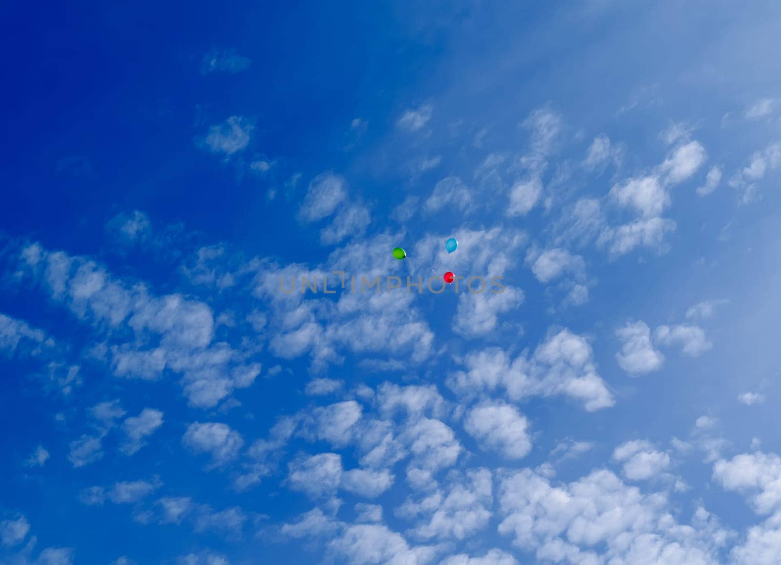 Three multi-colored balloons fly (hover) in the blue sky with clouds