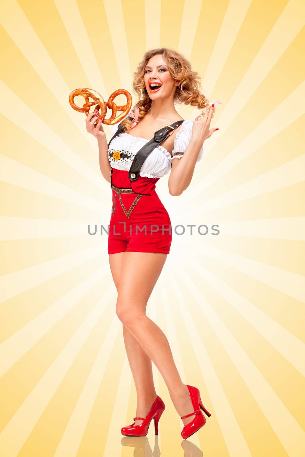 Beautiful sexy Oktoberfest woman wearing red jumper shorts with suspenders in a form of a traditional dirndl, holding two pretzels on colorful abstract cartoon style background.