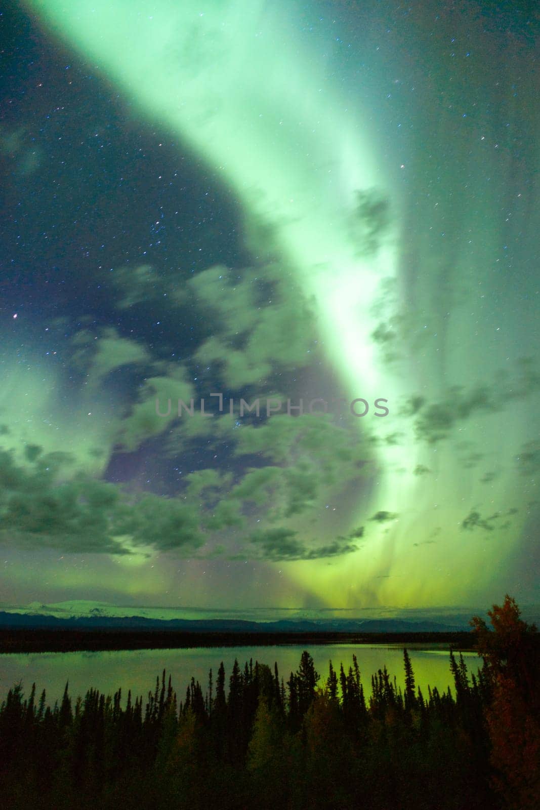The Northern Lights emerge through the clouds in remote Alaska