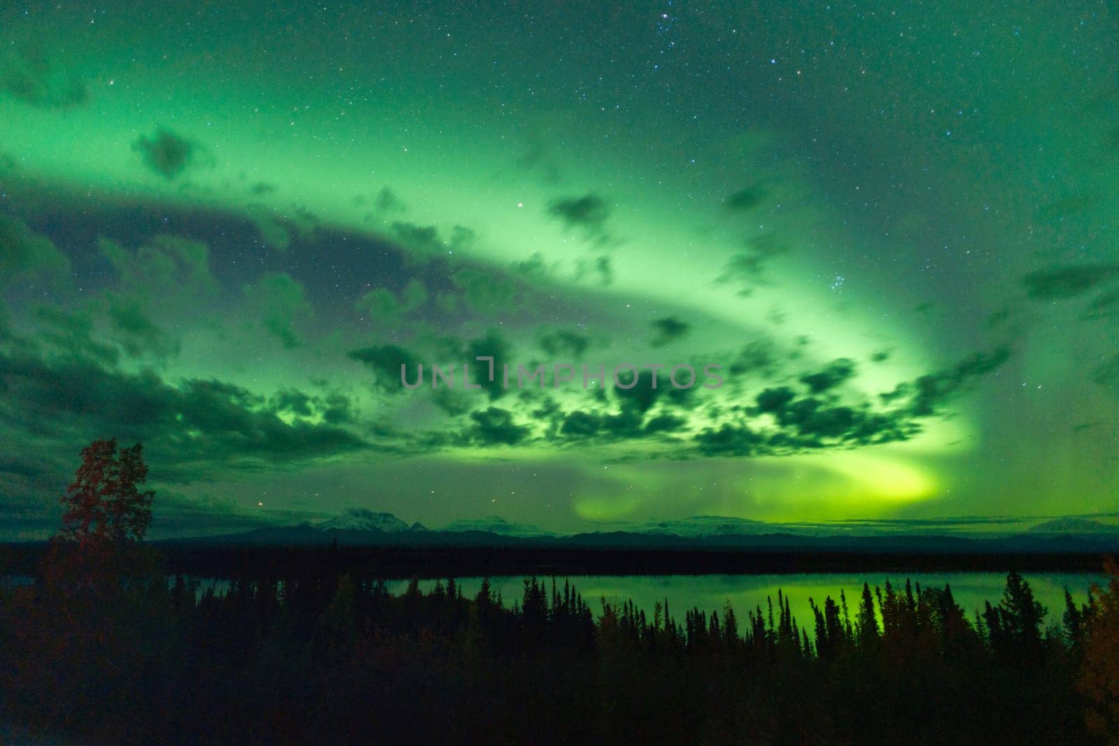 The Northern Lights emerge through the clouds in remote Alaska