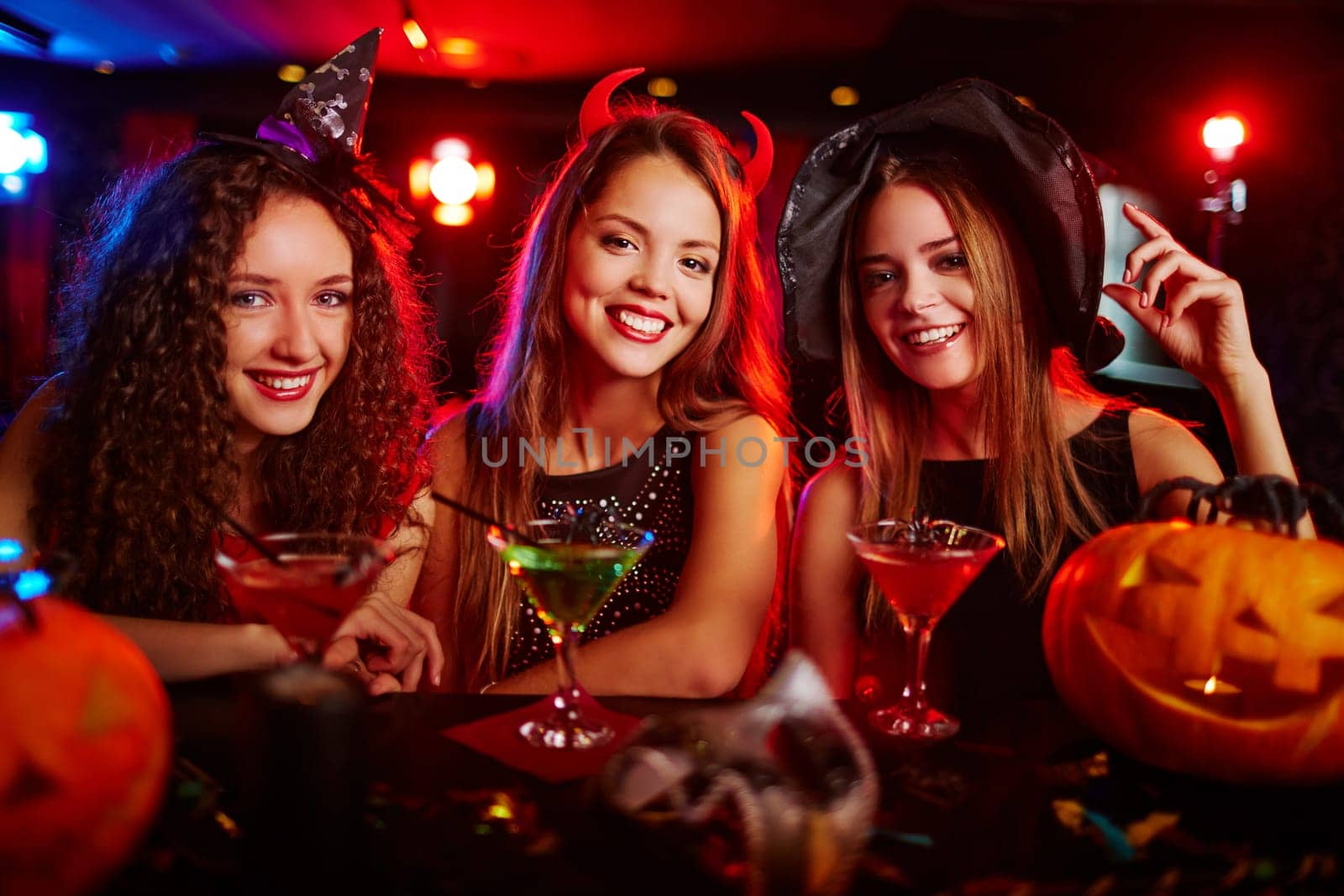 Happy young witches drinking cocktails at bar counter