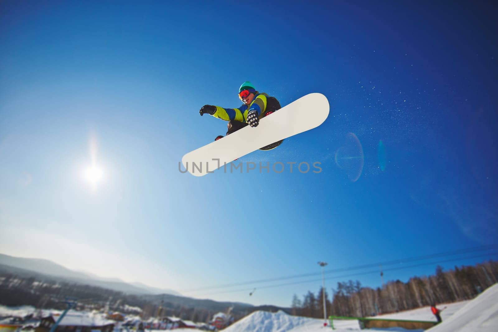 Active young man snowboarding against blue sky