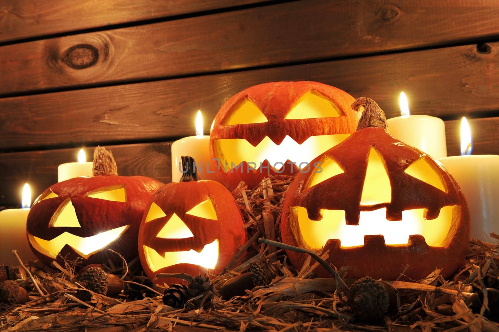 Four illuminated Halloween pumpkins with straw in front of old weathered wooden boards in candlelight