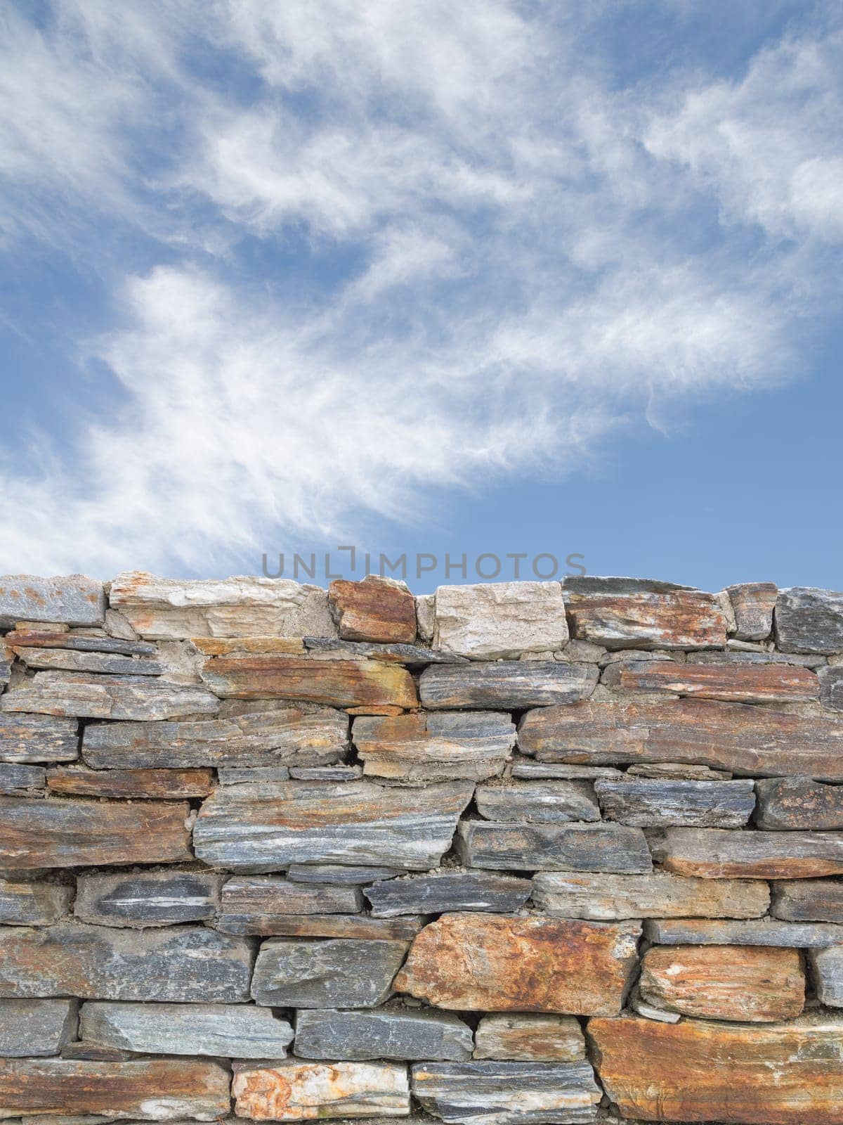 Vertical background with rough stone texture masonry wall and blue cloudy sky