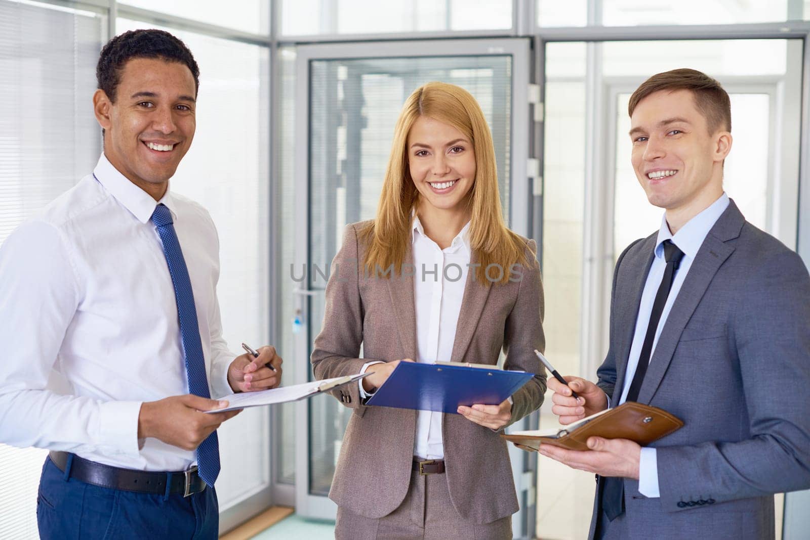 Happy business team in formalwear looking at camera in office