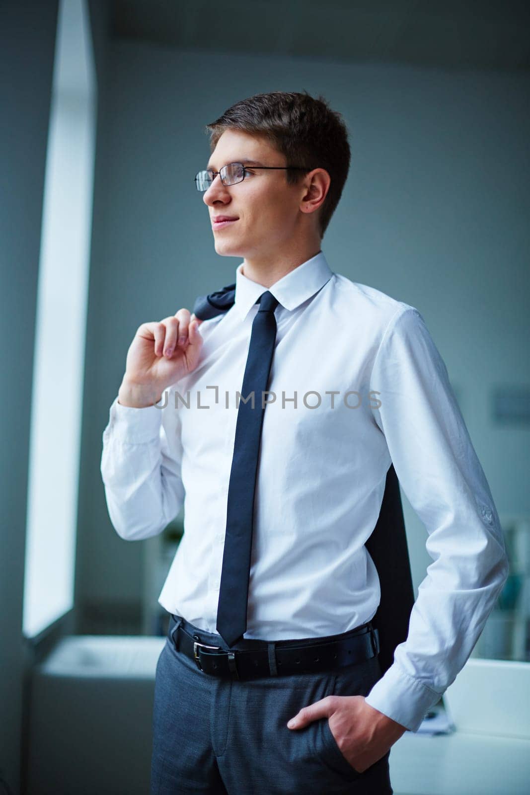 Young elegant businessman standing by window in office