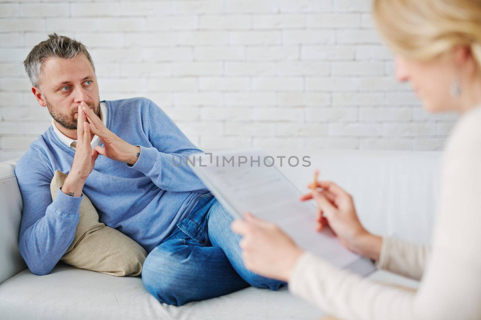 Thoughtful man sitting on sofa in front of his psychologist