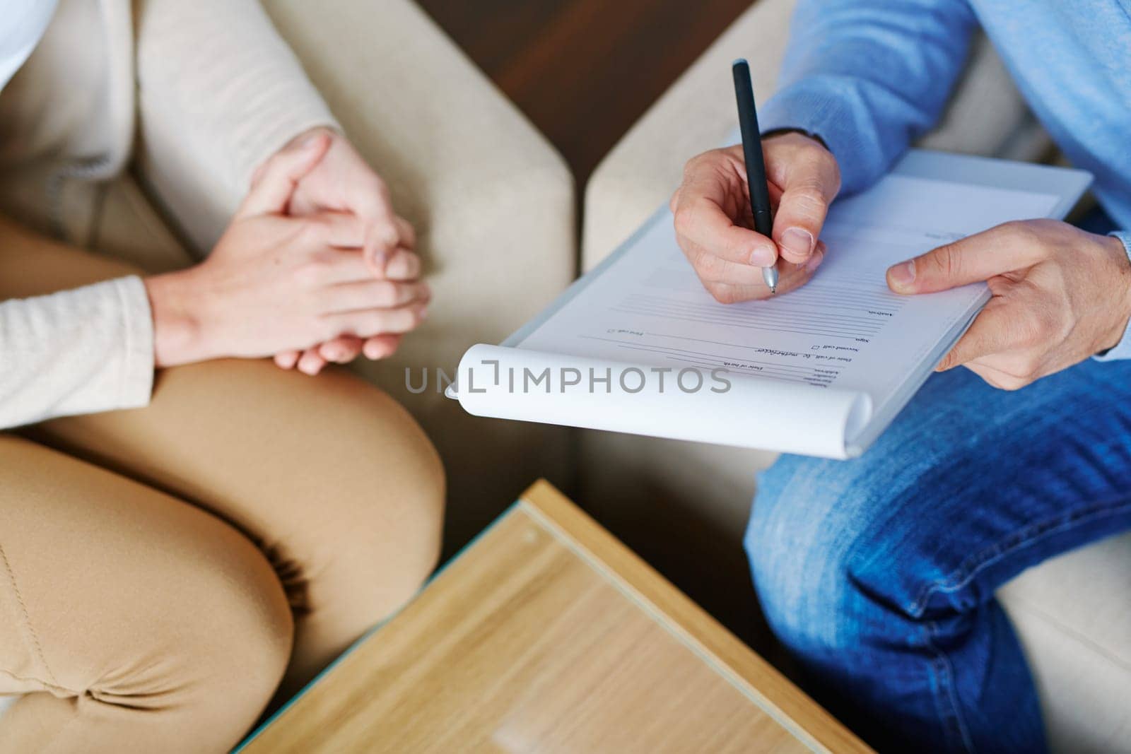 Hands of psychiatrist filling in medical document with patient near by