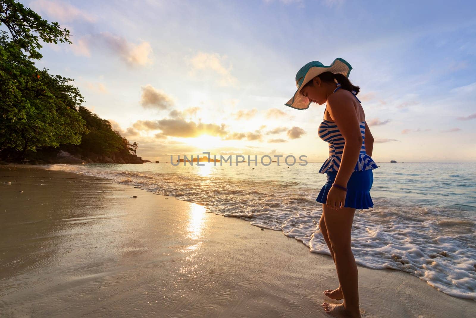 Girl in a swimsuit standing sand and water play with happiness during sunrise on the beach of Honeymoon Bay at Koh Miang, Similan Islands National Park, Phang Nga, Thailand