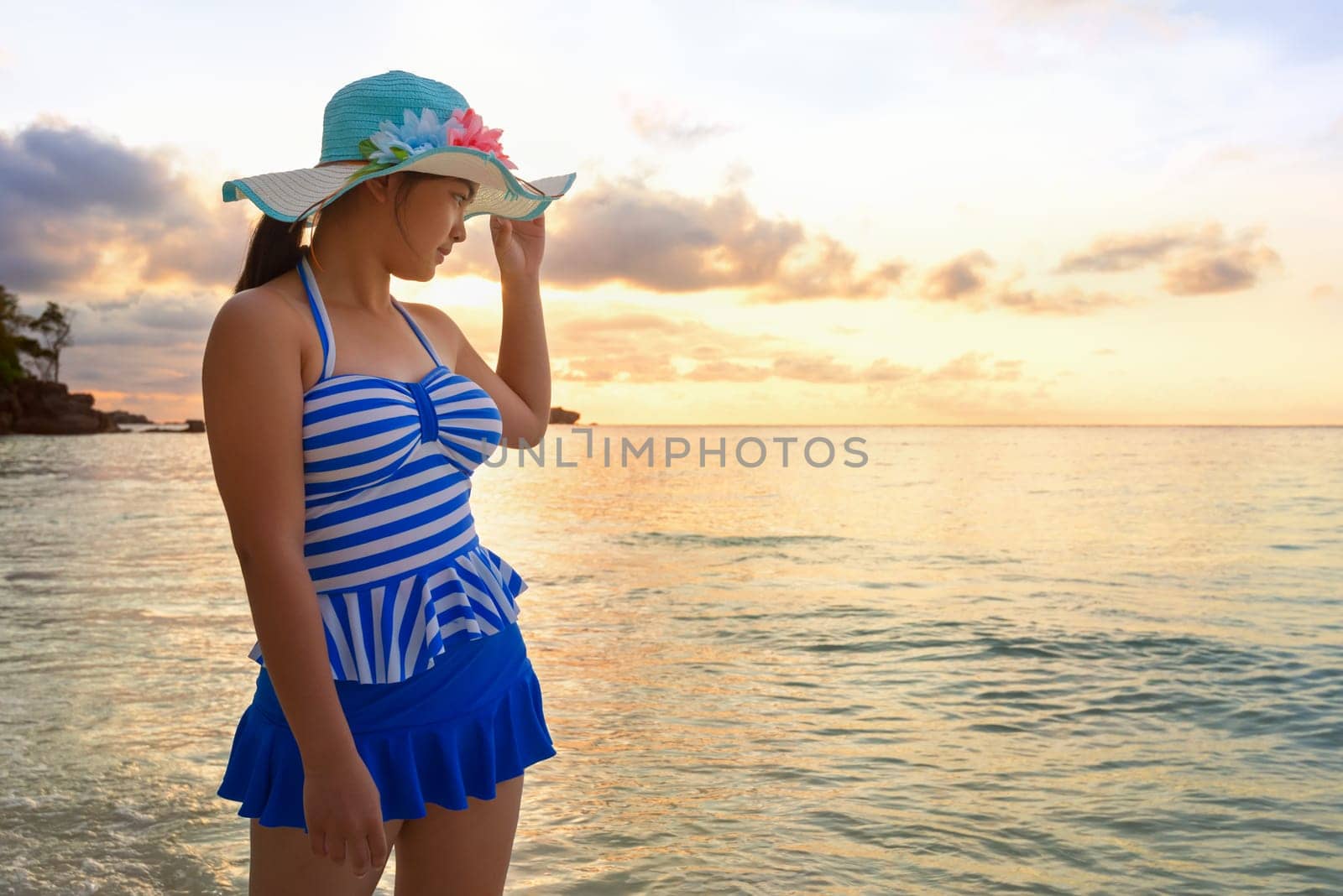 Woman in swimsuit standing poses on beach with happy and beautiful sky above the sea during sunrise at Honeymoon Bay, Koh Miang Island, Similan National Park, Phang Nga, Thailand