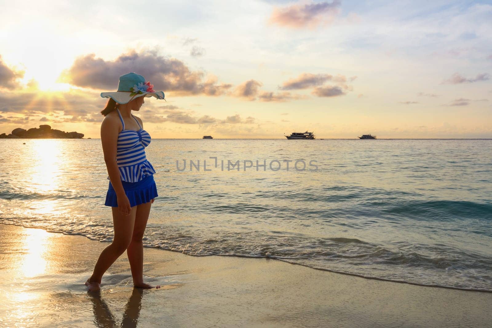 Girl in blue swimsuit walking on beach with happy and beautiful sky above the sea during sunrise at Honeymoon Bay, Koh Miang Islands, Similan National Park, Phang Nga, Thailand