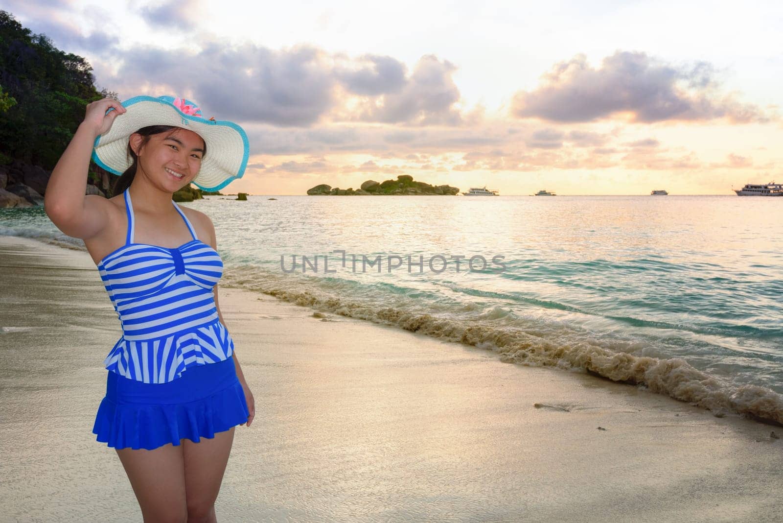 Woman in swimsuit standing poses on beach with happy and beautiful sky above the sea during sunrise at Honeymoon Bay, Koh Miang Island, Similan National Park, Phang Nga, Thailand