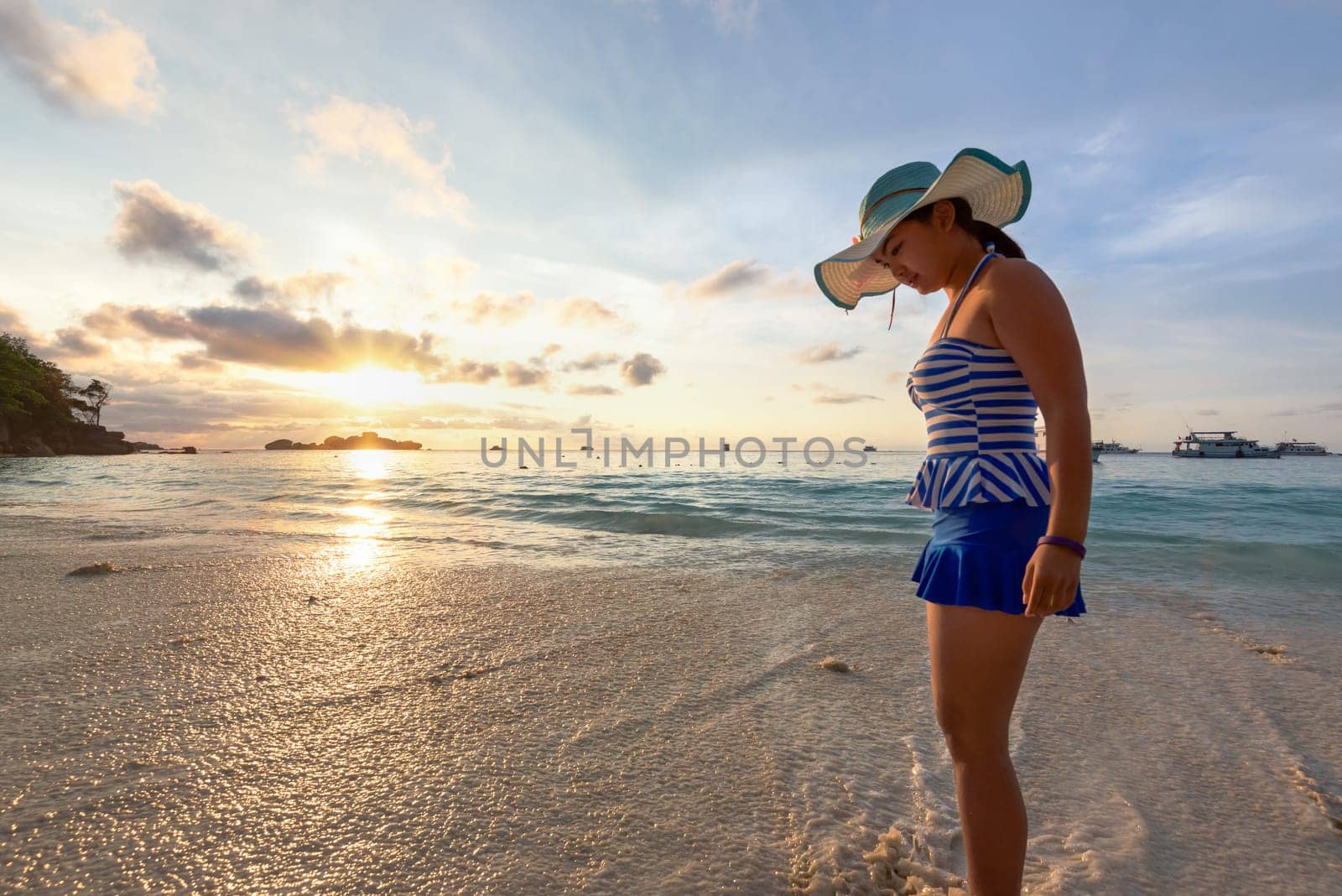 Girl in a swimsuit standing sand and water play with happiness during sunrise on the beach of Honeymoon Bay at Koh Miang, Similan Islands National Park, Phang Nga, Thailand