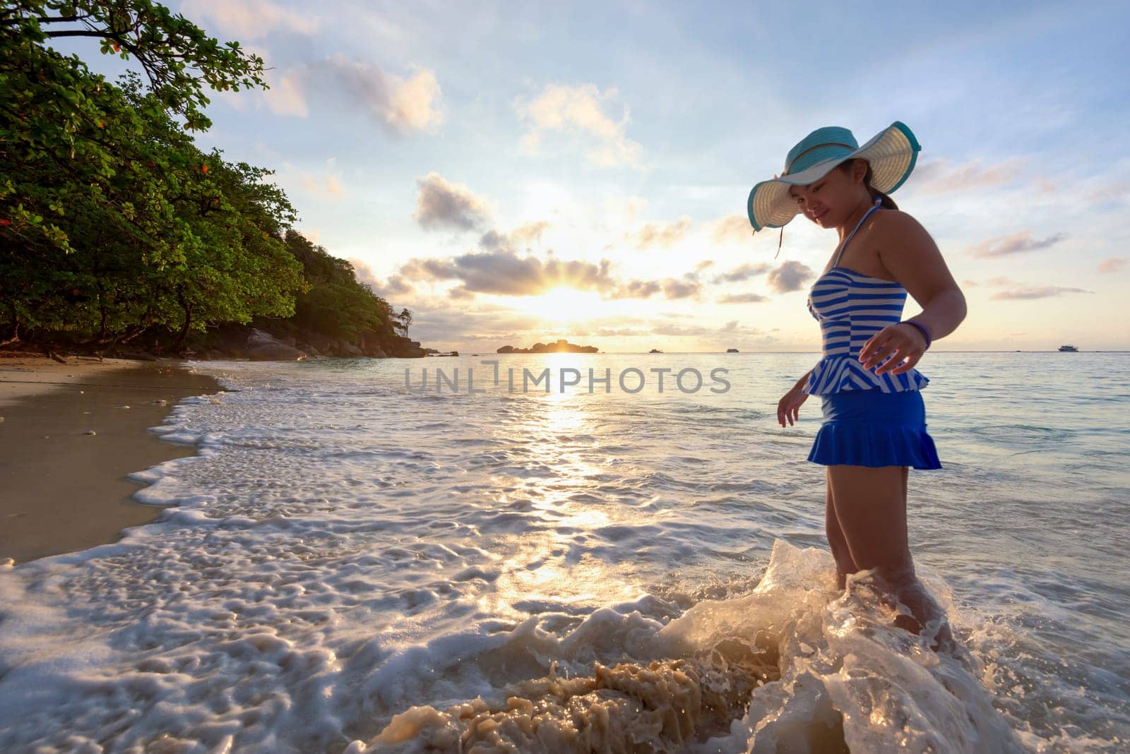 Girl in a swimsuit standing sand and water play with happiness during sunrise on the beach of Honeymoon Bay at Koh Miang, Similan Islands National Park, Phang Nga, Thailand