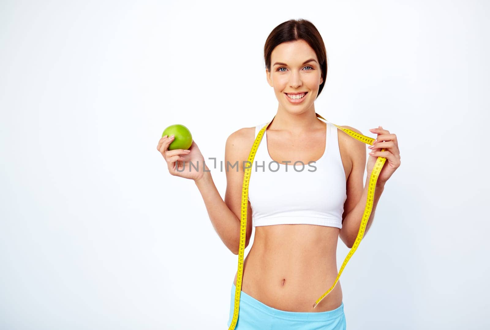 Active young female with green apple and measuring tape looking at camera