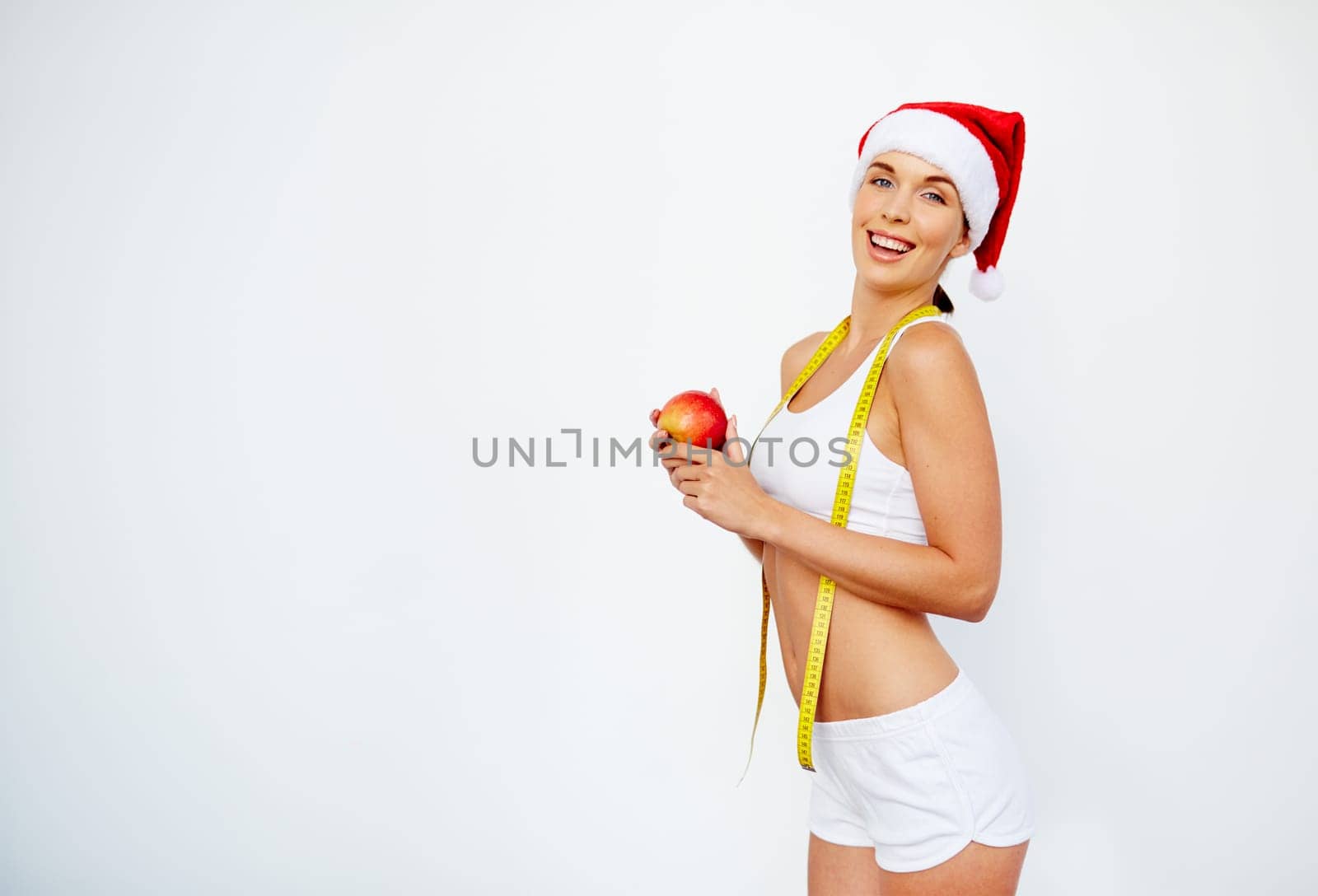 Young woman with slim figure in Santa cap holding red apple and measuring tape