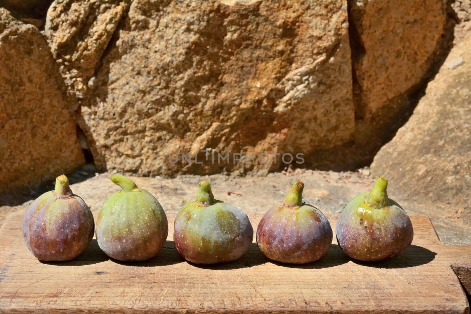 Composition of fig fruits on a wooden board and rocks in the background.