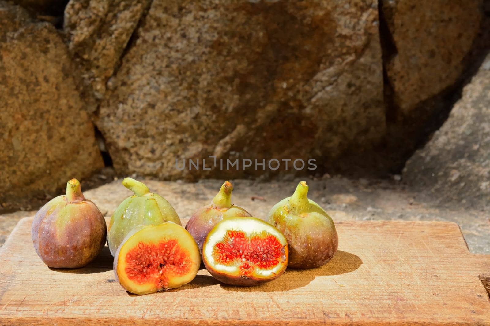 Composition of fig fruits on a wooden board and rocks in the background.