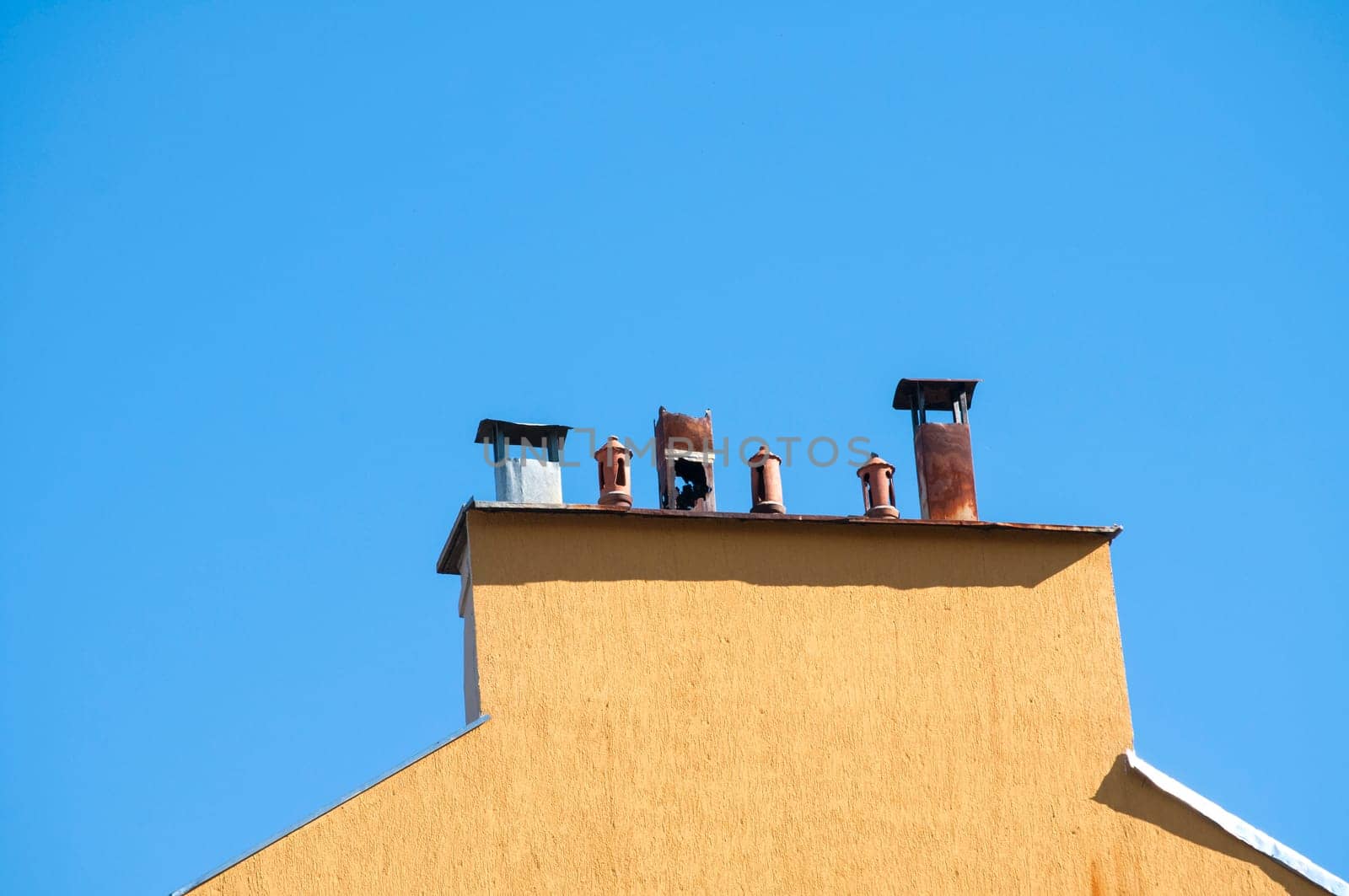 Chimney section of yellow house wall with different chimney caps on blue sky background