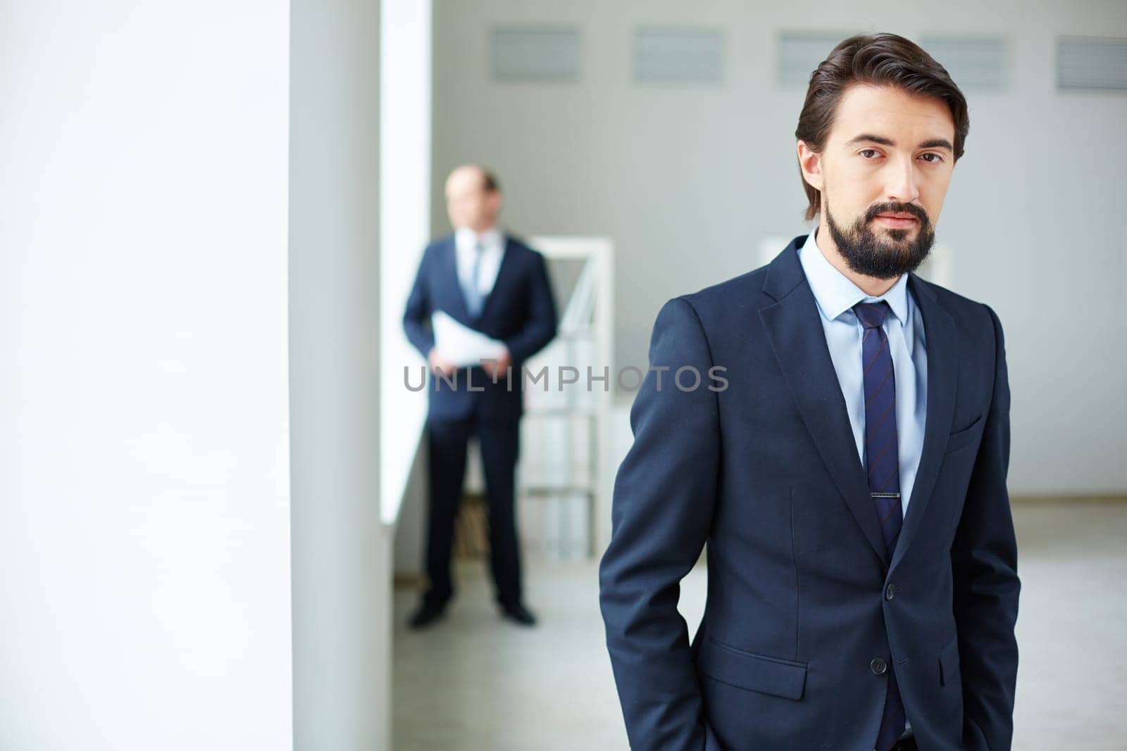 Elegant businessman looking at camera on background of his colleague