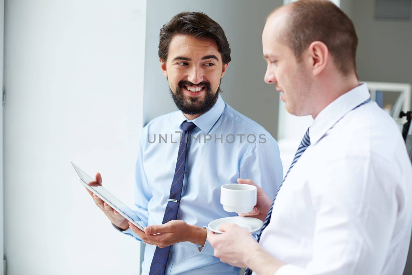 Young businessman with touchpad showing data to his colleague at meeting