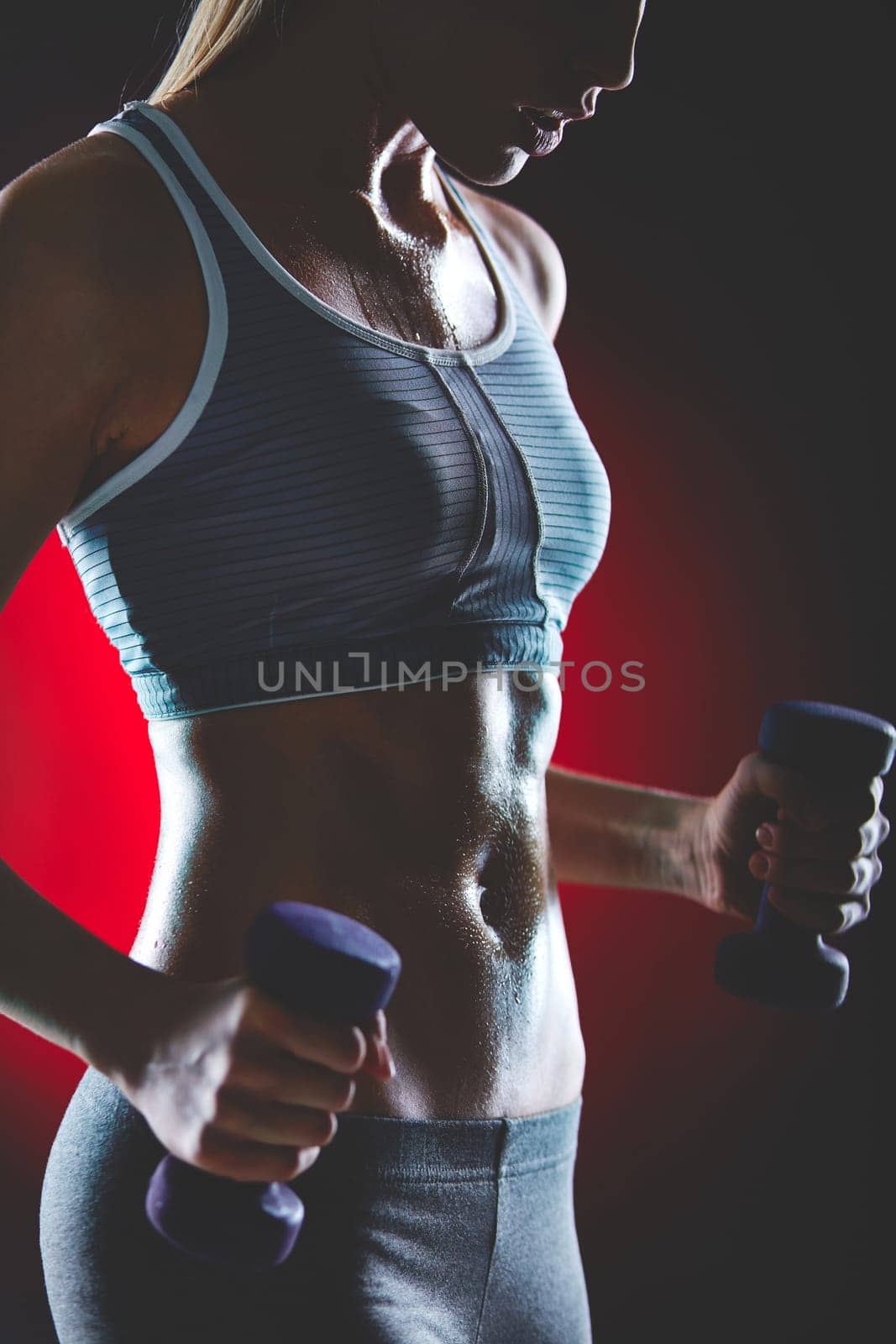 Young female doing exercise with dumbbells and sweating