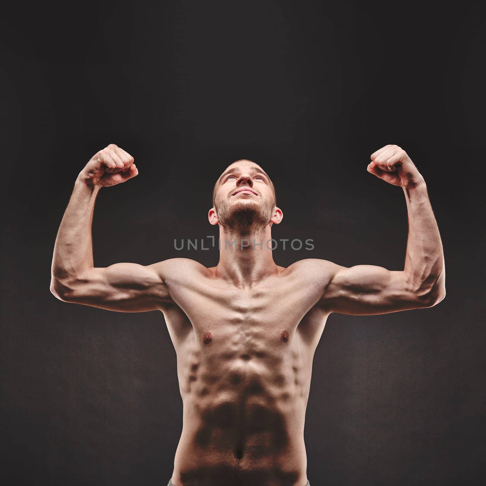 Strong young man looking upwards with raised arms in isolation