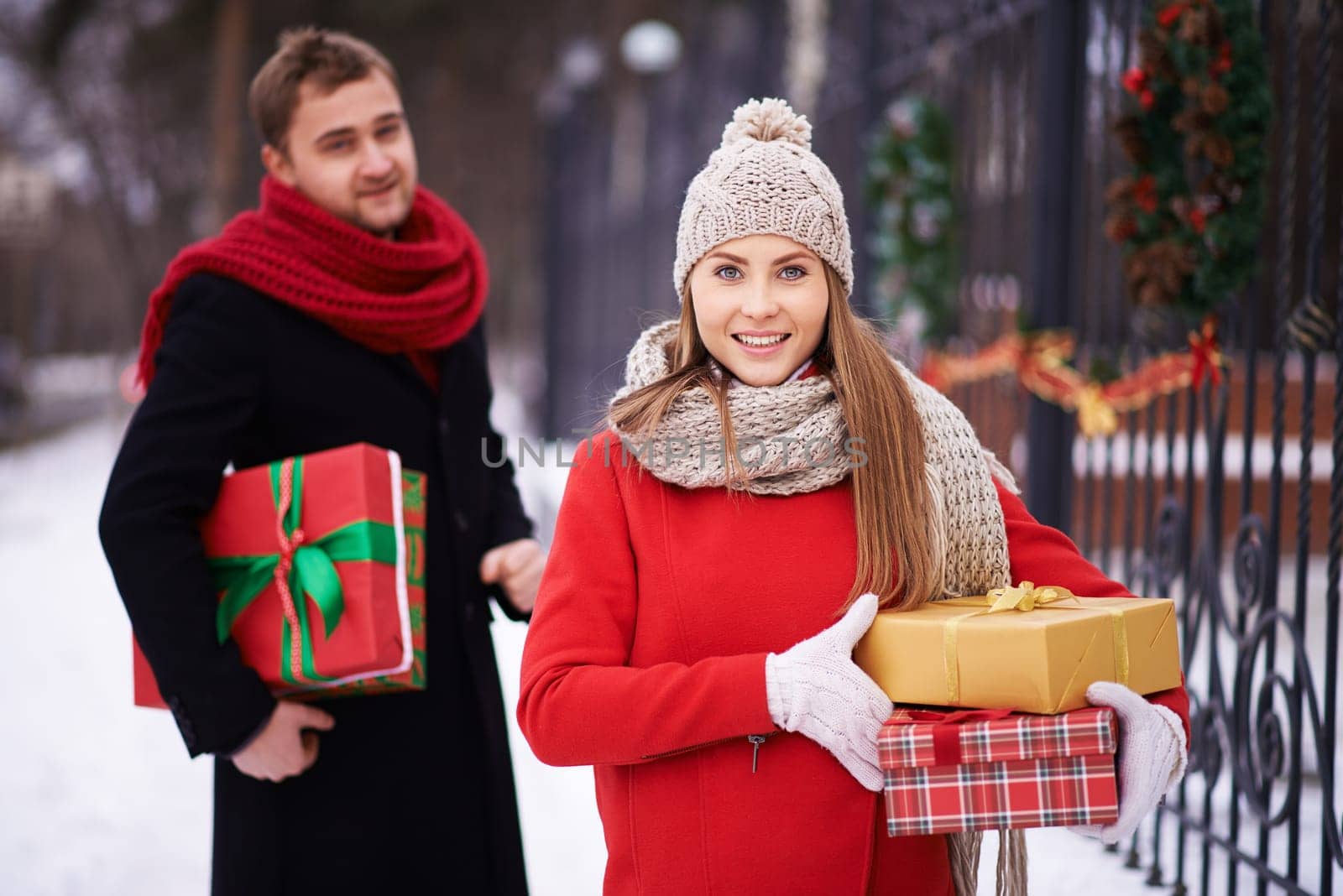 Happy woman with Christmas presents looking at camera on background of her husband outdoors