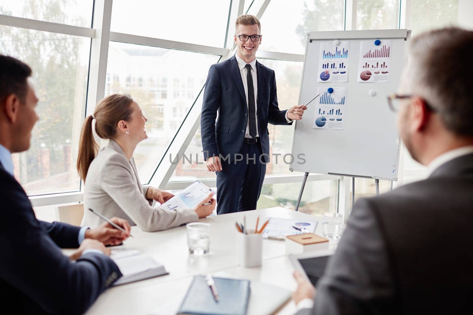 Happy colleagues looking at confident young businessman pointing at chart on board