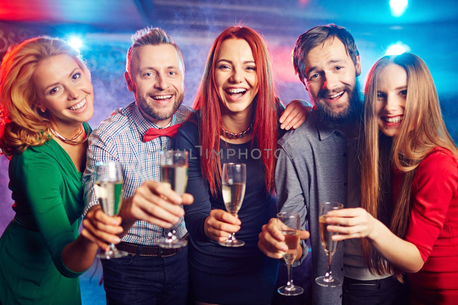 Cheerful friends with flutes looking at camera at party in night club