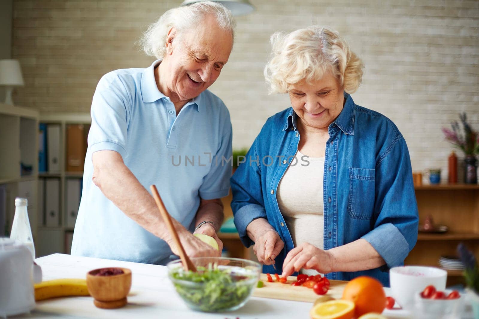 Happy senior couple preparing fresh vegetable salad in the kitchen