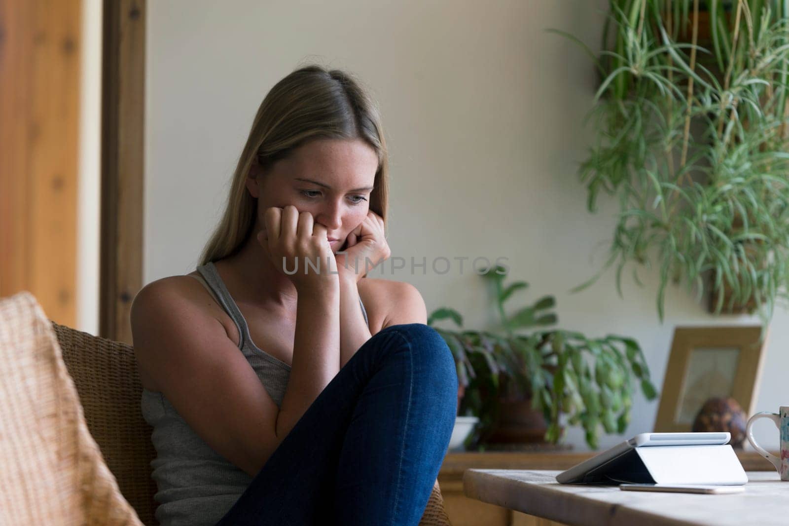 Woman at home looking stressed at her dining room table. She has a digital tablet and a smartphone in front of her.