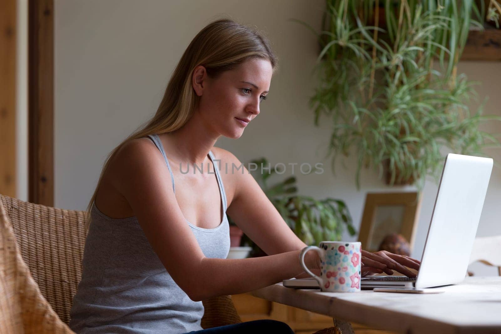 Woman sitting in her home using a laptop whilst enjoying a cup of tea.