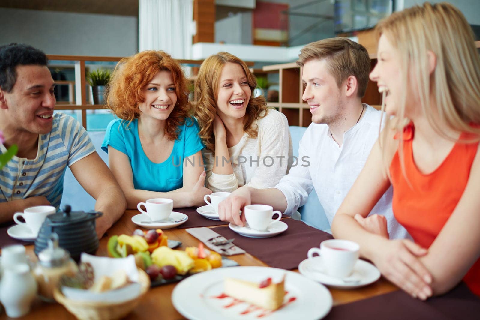 Happy friends relaxing and having tea with snack in cafe
