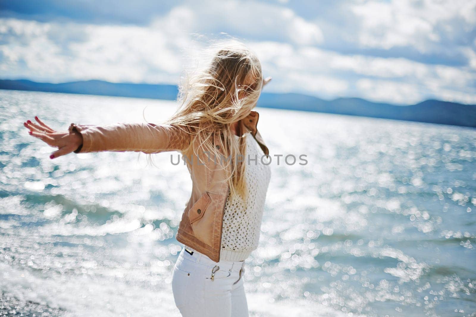 Happy long-haired girl standing with outstretched arms by the seaside