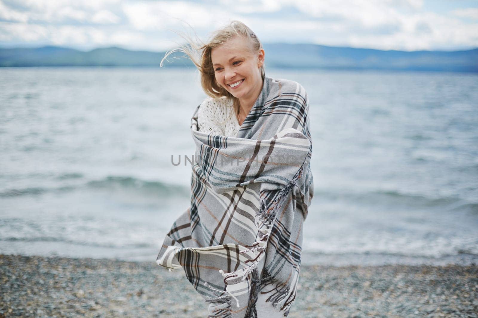 Young woman wrapped in plaid standing by the seaside