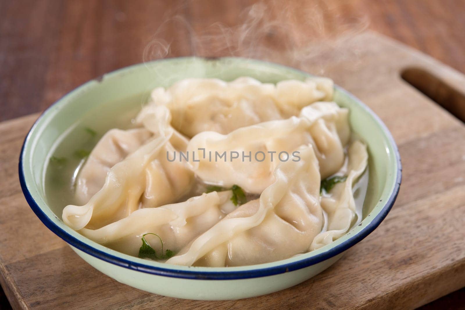 Fresh dumplings soup on plate with hot steams. Chinese cuisine on rustic old wooden background.